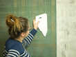 girl gluing wallpaper at home, smoothing out new wallpaper with a plastic spatula