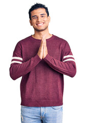 Canvas Print - Hispanic handsome young man wearing casual clothes praying with hands together asking for forgiveness smiling confident.