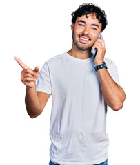 Canvas Print - Hispanic young man with beard having conversation talking on the smartphone smiling happy pointing with hand and finger to the side