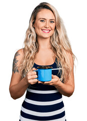 Poster - Young blonde woman drinking a cup of coffee looking positive and happy standing and smiling with a confident smile showing teeth