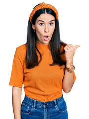 Wall Mural - Young hispanic woman wearing casual clothes surprised pointing with hand finger to the side, open mouth amazed expression.