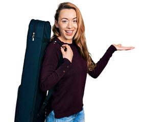 Wall Mural - Young caucasian woman wearing guitar case celebrating achievement with happy smile and winner expression with raised hand