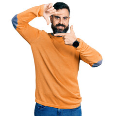 Wall Mural - Hispanic man with beard wearing casual winter sweater smiling making frame with hands and fingers with happy face. creativity and photography concept.