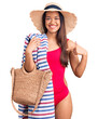 Young beautiful latin girl wearing swimwear and summer hat holding beach towel and bag pointing finger to one self smiling happy and proud