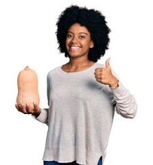 Poster - Young african american woman holding healthy fresh pumpkin smiling happy and positive, thumb up doing excellent and approval sign