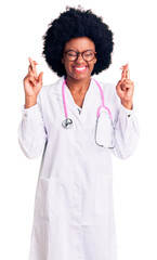 Poster - Young african american woman wearing doctor coat and stethoscope gesturing finger crossed smiling with hope and eyes closed. luck and superstitious concept.