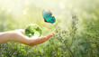 Earth Day or World Environment Day, environmentally friendly theme. Morpho butterfly and Crystal globe ball in hand on green leaves background. Save planet and protect nature, sustainability concept.