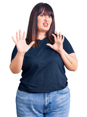 Canvas Print - Young plus size woman wearing casual clothes afraid and terrified with fear expression stop gesture with hands, shouting in shock. panic concept.