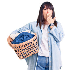 Wall Mural - Young plus size woman holding laundry basket covering mouth with hand, shocked and afraid for mistake. surprised expression