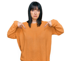 Canvas Print - Young hispanic woman wearing casual clothes pointing down looking sad and upset, indicating direction with fingers, unhappy and depressed.