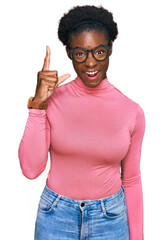 Wall Mural - Young african american girl wearing casual clothes and glasses pointing finger up with successful idea. exited and happy. number one.