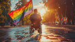 © Sophie  - Dsabled gay person in wheelchair with rainbow flag on street parade during pride month celebration LGBTQ+ rights party summer festival. Inclusion & diversity. Autumn trees, golden hour sun. Rear view.
