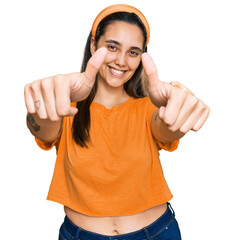 Wall Mural - Young hispanic woman wearing casual clothes approving doing positive gesture with hand, thumbs up smiling and happy for success. winner gesture.