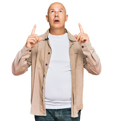 Wall Mural - Middle age bald man wearing casual clothes amazed and surprised looking up and pointing with fingers and raised arms.