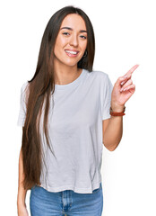 Sticker - Young hispanic girl wearing casual white t shirt with a big smile on face, pointing with hand finger to the side looking at the camera.