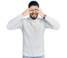 Wall Mural - Young arab man with beard wearing elegant turtleneck sweater and glasses covering eyes with hands smiling cheerful and funny. blind concept.