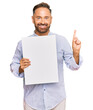 © Krakenimages.com - Handsome middle age man holding blank empty banner surprised with an idea or question pointing finger with happy face, number one