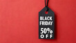 Photo of hanging black price tag on isolated red background with text black friday 50% off