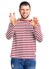 Sticker - Young handsome man wearing striped sweater smiling funny doing claw gesture as cat, aggressive and sexy expression