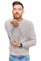 Wall Mural - Young redhead man wearing casual winter sweater looking at the camera blowing a kiss with hand on air being lovely and sexy. love expression.