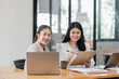 © Mongta Studio - Two smiling female professionals engaged in a productive business meeting with laptops and paperwork in an office.