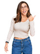 © Krakenimages.com - Young brunette woman wearing casual clothes and glasses smiling with happy face looking and pointing to the side with thumb up.