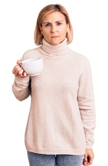 Wall Mural - Young blonde woman holding coffee thinking attitude and sober expression looking self confident