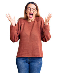 Wall Mural - Beautiful young woman wearing casual clothes and glasses celebrating crazy and amazed for success with arms raised and open eyes screaming excited. winner concept