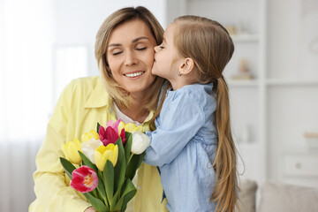 Poster - Little daughter kissing and congratulating her mom with Mother`s Day at home. Woman holding bouquet of beautiful tulips