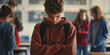a depressive boy bowed her head down and stands in the middle of a classroom at school. Bullying at school.