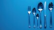 Silver cutlery set aligned on blue background, including fork, spoons, and knife