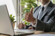 © antusher - A man in a suit is giving a thumbs up while sitting at a desk with a laptop