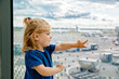 Cute little toddler girl at the airport, traveling. Happy healthy child waiting near window and watching airplanes. Family going on summer vacations by plane.