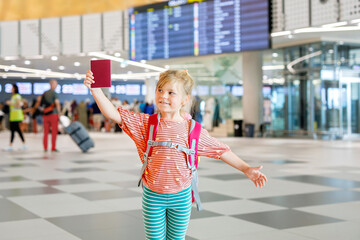 Little preschool girl at airport terminal. Happy child going on vacations by airplane. Smiling kid with passport and bag.