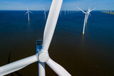 Fototapeta  - A group of wind turbines gracefully spinning in the ocean, harnessing the power of the wind in Flevoland, Netherlands during the vibrant season of Spring. Windmill turbines green energy in the ocean