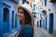 A young woman on travel vacation is enthralled by the sights of vibrant, colorful houses on the streets of Chefchaouen, Morocco. A female tourist sightseeing, enjoying her visit to the 'Blue City'.