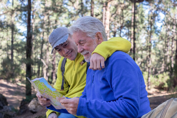 Wall Mural - Young grandson and old grandfather consulting trail map while hiking in mountain forest enjoying nature and healthy activity. The new and old generation share the same passion. Adventure has no age