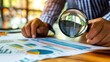 A person holding a magnifying glass over positive indicators on a financial report, symbolizing careful analysis and scrutiny.