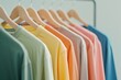 A rack with casual t-shirts hanging on wooden hangers, arranged in an organized and stylish manner against a white background. The shirts come in various colors including pastel