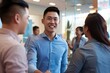 A young happy Asian man in a blue shirt shaking hands with a business person