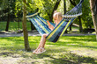 Cute 5 years old girl lounging in a hammock, enjoying the warm summer day in a picturesque park while holding a smartphone and wearing kids sunglasses.