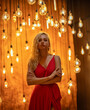 Beautiful blonde woman in long red dress posing with Edison LED lamps in retro style that lights brightly with warm light.