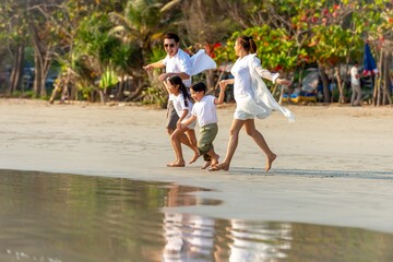 Wall Mural - Happy Asian family travel nature ocean on summer holiday vacation. Parents and little child kid enjoy and fun outdoor activity lifestyle walking and playing together on tropical island beach at sunset