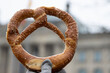 Hand holding Appetizing traditional Bavarian pretzel with the salt crystals. The Berlin Reichstag building can be seen through the bretzel on the blurred  background. Symbol of Germany, Bavaria.