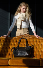 Wall Mural - beautiful curly blond hair woman posing with a small black shopper bag near vintage volor sofa