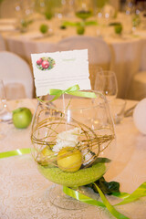 Wall Mural - Vertical shot of a glass vase with green sand, apples and flowers on a wedding event