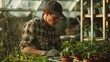 Young man gardening, deeply focused on nurturing plants in a greenhouse.