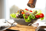 Fototapeta Tulipany - Fresh green salad in a ceramic bowl with tomato, onions and olives on wooden cutting board. Healthy nutrition concept for fitness and spring diet. Close-up.