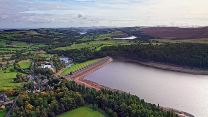 Wall Mural - Drone footage of lake by lush green fields and trees in Langsett Reservoir, England with gray sky