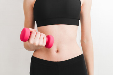 young beautiful caucasian teen girl in a fitness suit holds pink dumbbell with one hand .